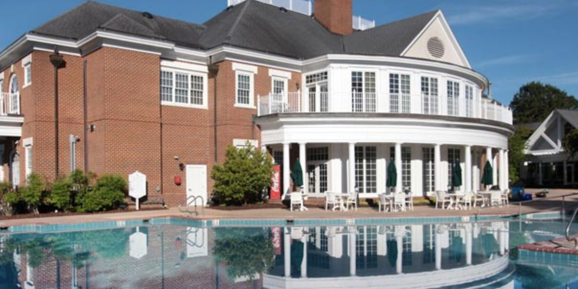 A large pool with chairs around it and a house in the background.